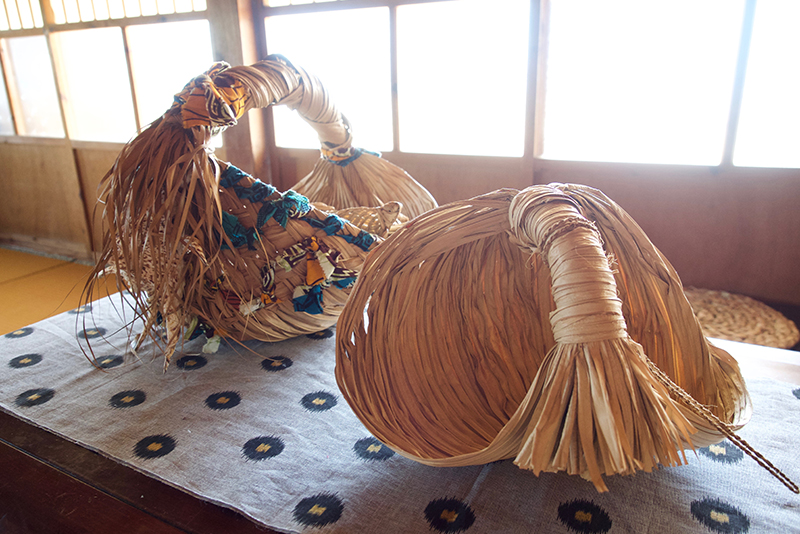是枝さんの作品。右はクバの葉でできた水くみかご。昔、井戸から水をくむ釣瓶（つるべ）などとして使われた「クバジー」や「ウブル」と呼ばれる沖縄の伝統民具にならって制作した。左は紅型やアフリカの布を編み込んだオリジナルのクバかご