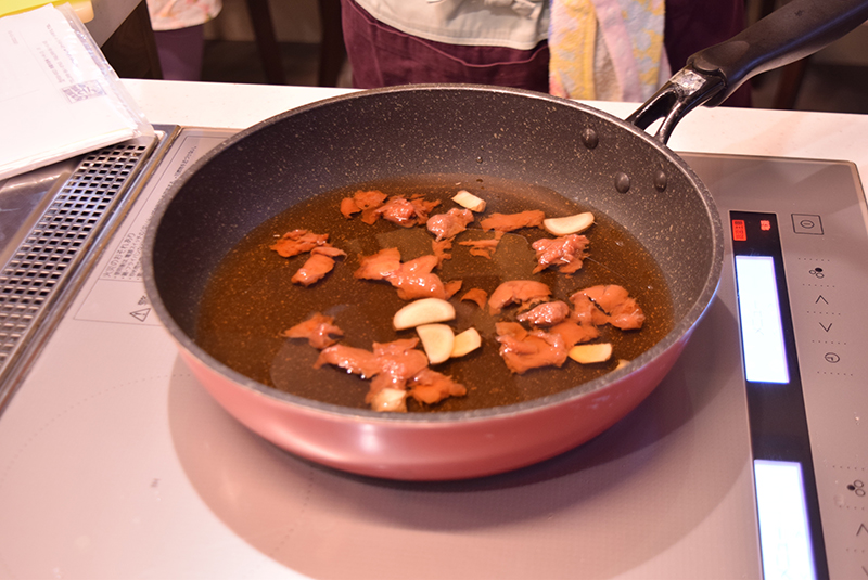 ２　サンマが一様に並ぶ鍋に、ショウガ、梅干し、煮汁の調味料を入れて煮立てる＝写真。