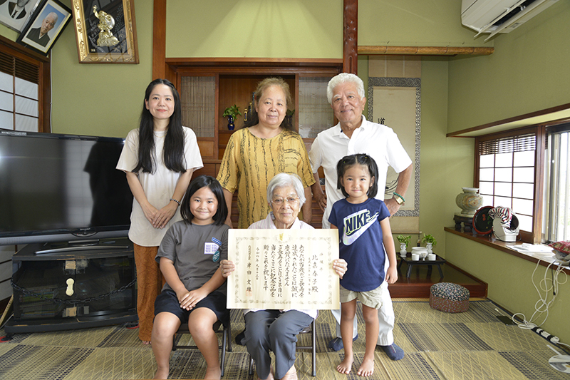 １００歳を祝い、岸田首相から贈られた賞状を手にする比嘉春子さん（前列中央）。子孫に囲まれ笑顔を見せる＝中城村の自宅