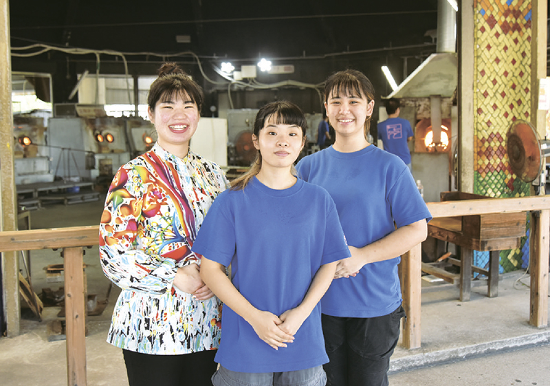 職人たちがガラス製品を作る工房の前に並ぶ伊敷美穂さん（左）、友寄琉花さん（中央）、天久琳々香さんの3人